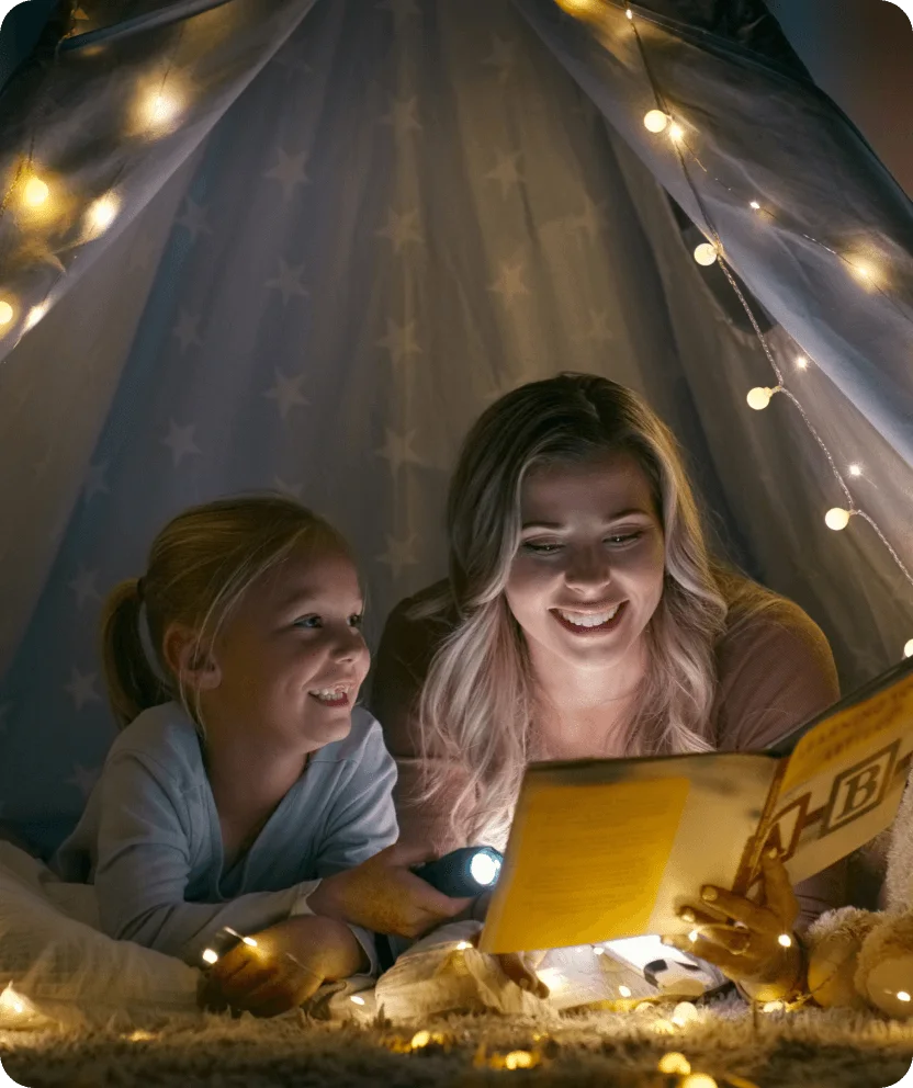 Children reading together under string lights in cozy tent