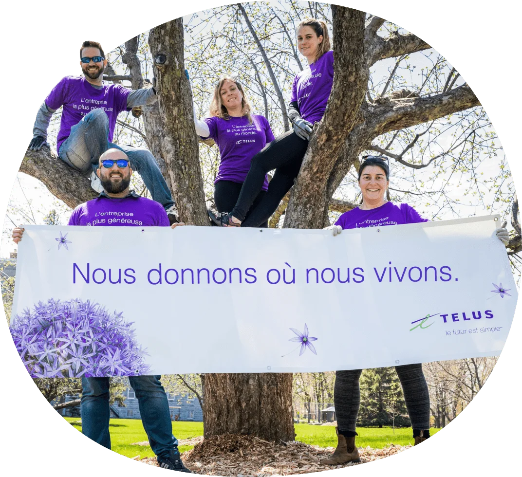 Cinq volontaires qui sont membres de l'équipe TELUS tiennent une banderole où il est écrit : Nous donnons où nous vivons.