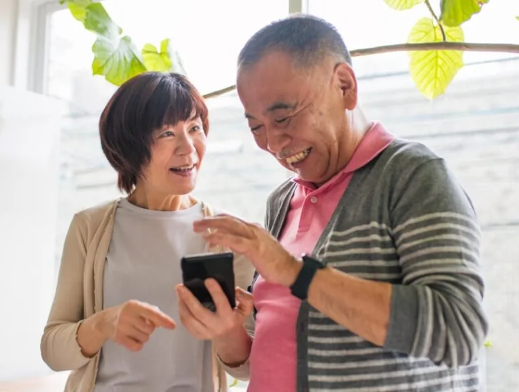 Un couple de personnes âgées partageant un rire tout en regardant un téléphone intelligent