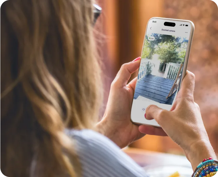 Femme tenant un téléphone intelligent qui affiche le flux de la caméra de sécurité résidentielle