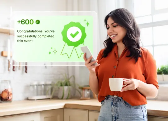 A person holds a smartphone and a coffee cup in a kitchen, with a pop-up message on the screen saying, "Congratulations! You've successfully completed this event" and "+600 points."