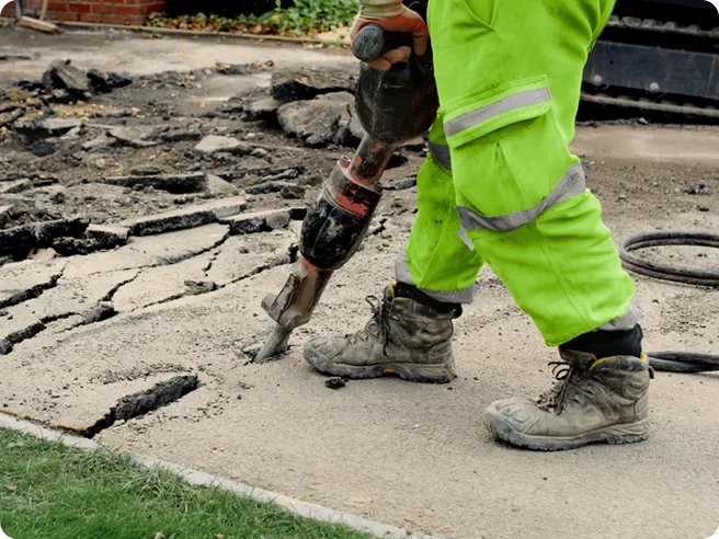 A construction worker is using a jackhammer to break up a sidewalk.