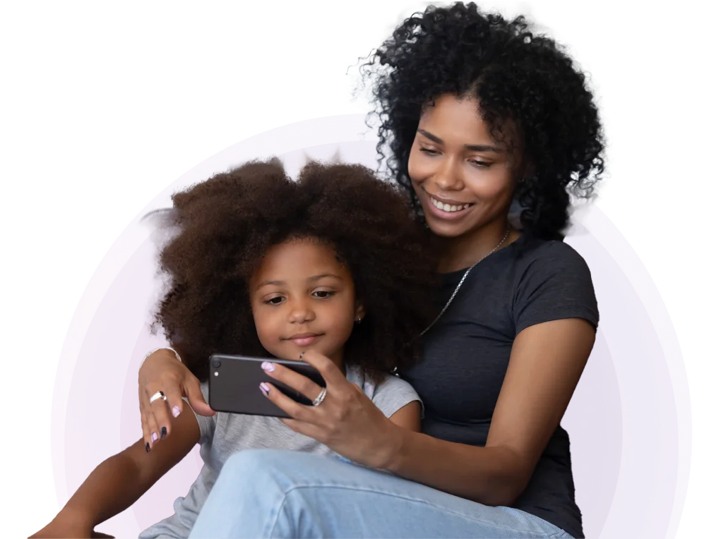 A woman with her arm around a child. They are both smiling and watching something on a smartphone that the woman is holding.