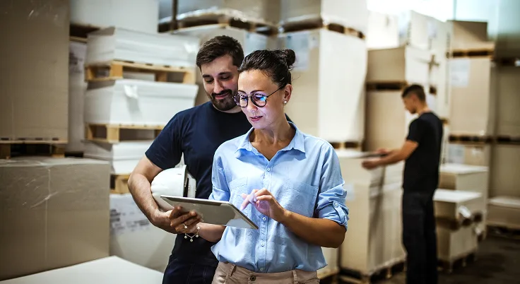 Warehouse workers using tablet for IT service management and inventory tracking.