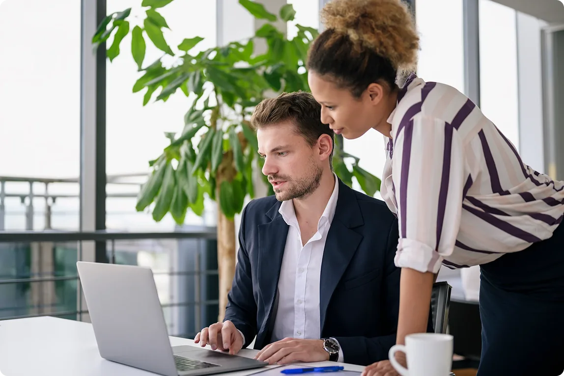 Two business professionals collaborating with ServiceNow on a laptop in a modern office.