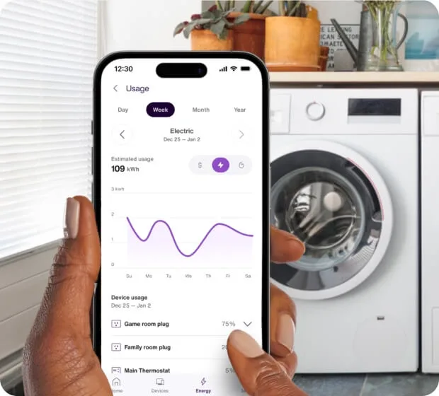 Hand holding smartphone showing appliance energy usage near washer/dryer
