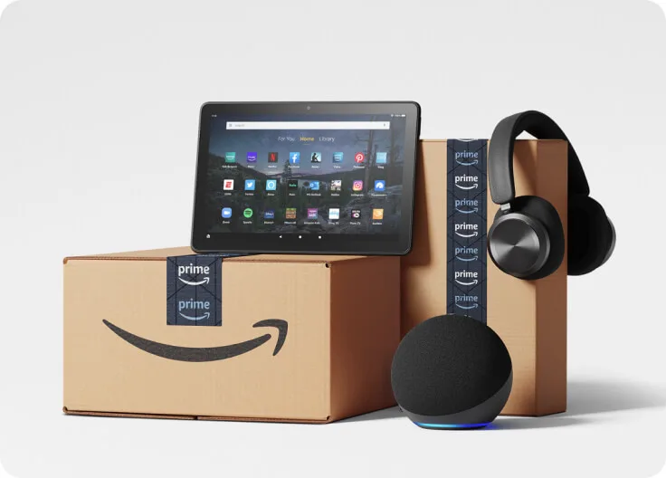 Amazon Prime branded products include, phone, Kindle e-reader, bag and box are in front of a TV with Jack Ryan show image.