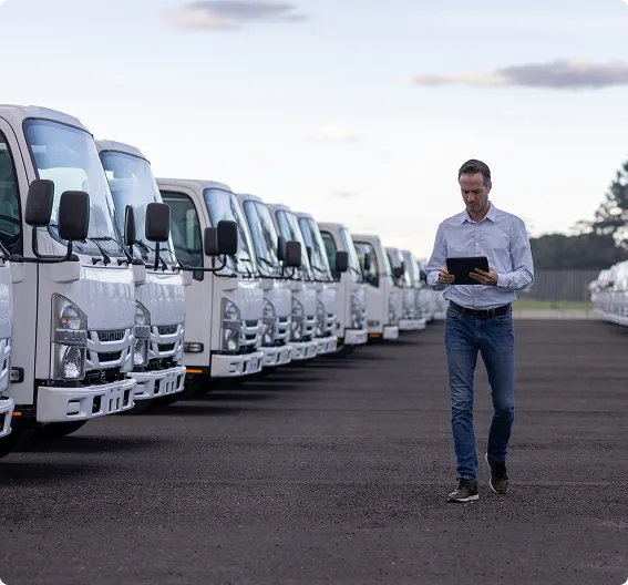 Raven fleet manager with tablet inspecting row of white commercial trucks.