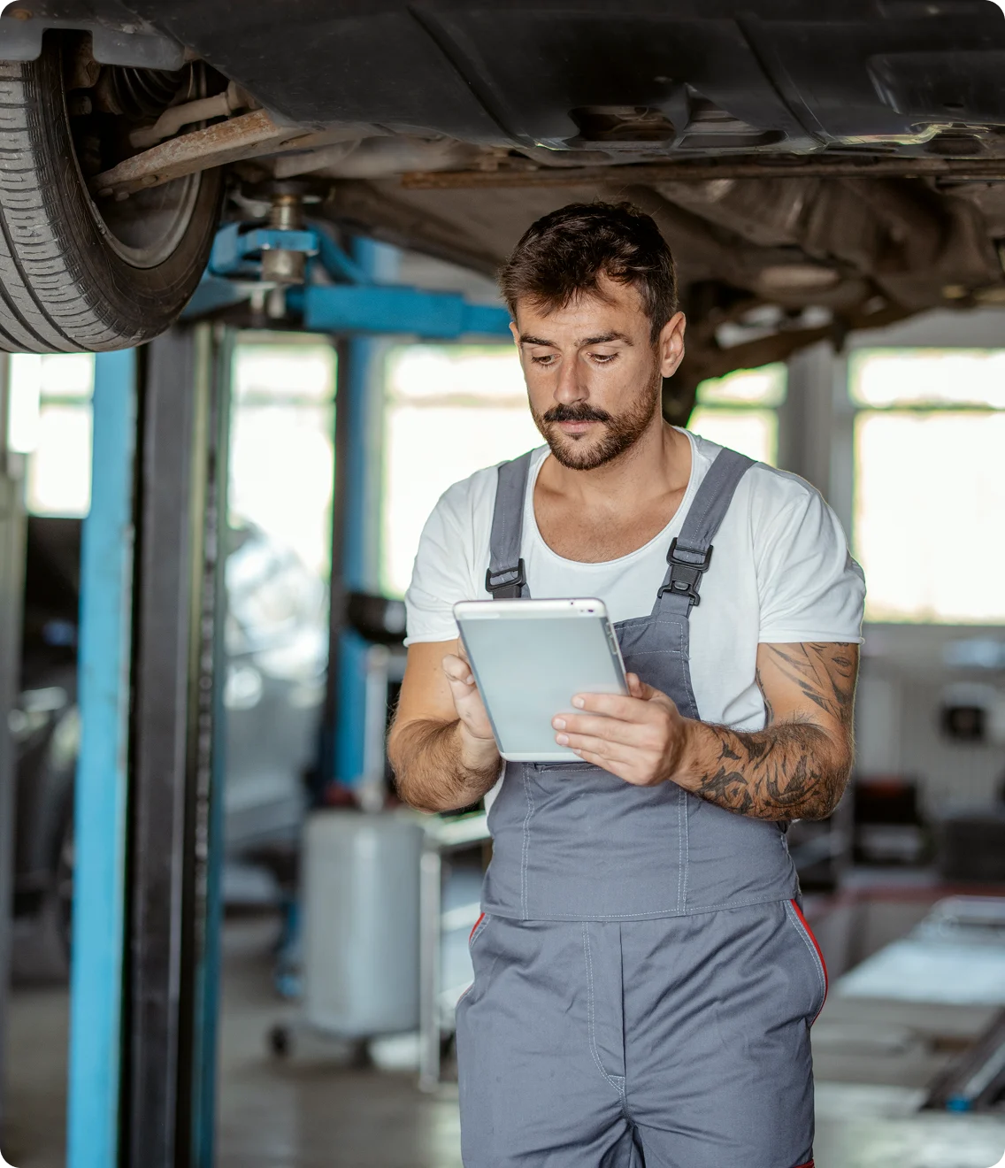 Auto technician under a hoist checks a tablet for service info.