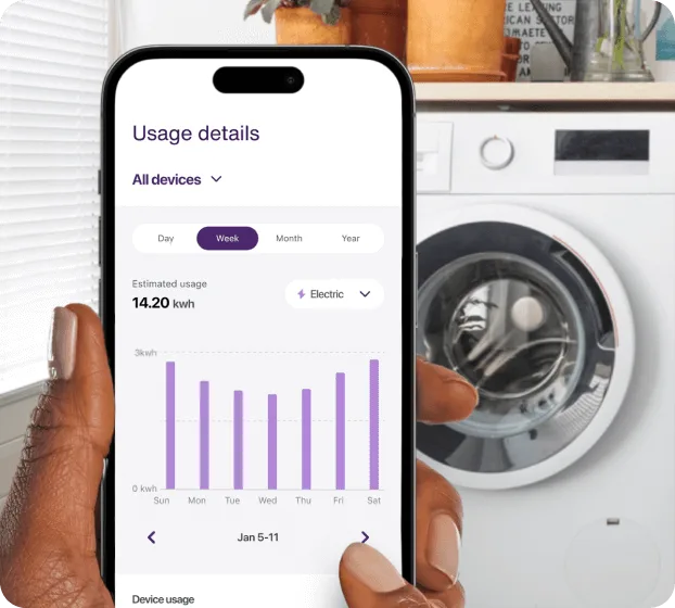 Hand holding smartphone showing appliance energy usage near washer/dryer