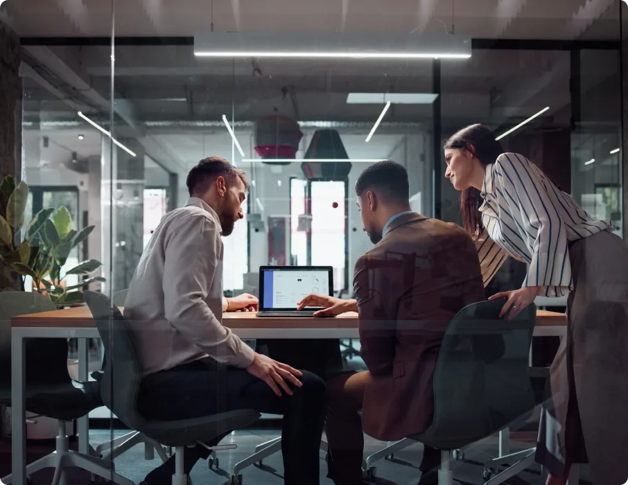 Professional meets with colleagues around a tablet in an office.
