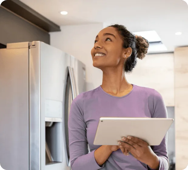 Woman with tablet in modern kitchen looking up thoughtfully