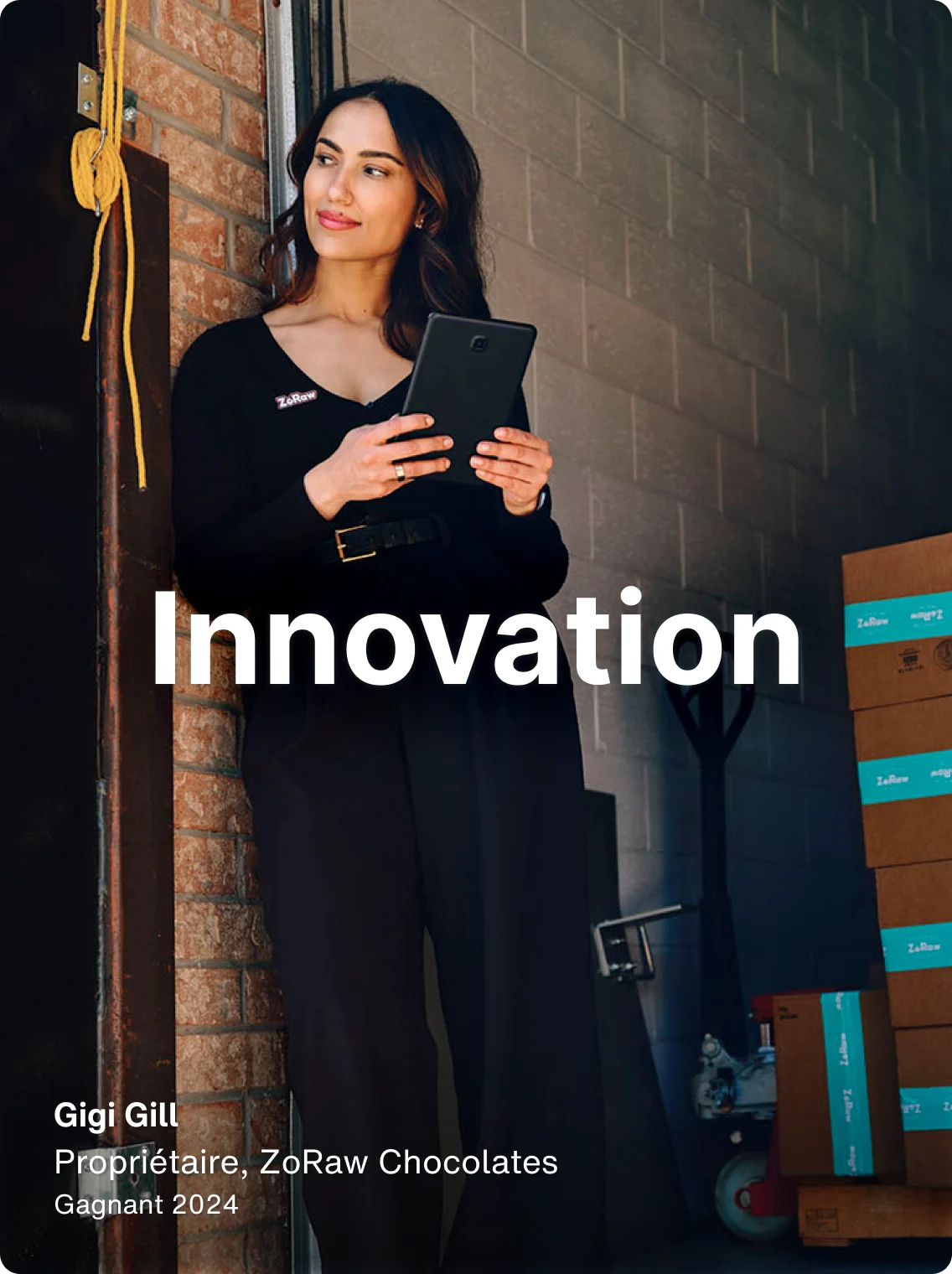 Gigi Gill, copropriétaire de ZoRaw Chocolates, adossée à un mur et tenant une tablette sur laquelle est superposé le mot « Innovation ».