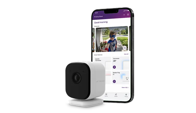 TELUS smart security camera next to a smartphone showing a live camera feed of a child in a costume on the app.
