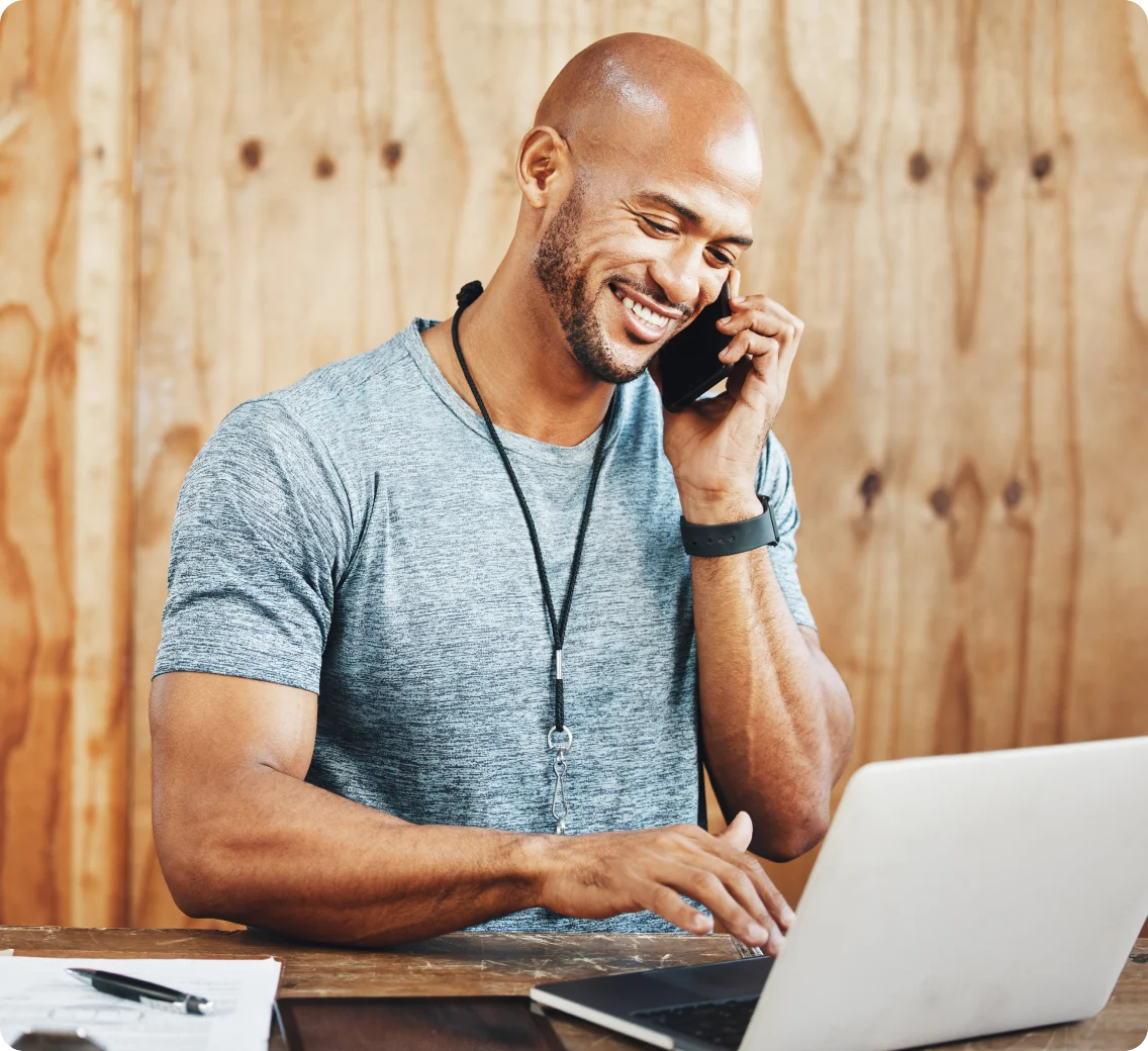 Fitness instructor smiles while taking a call and typing on a laptop.