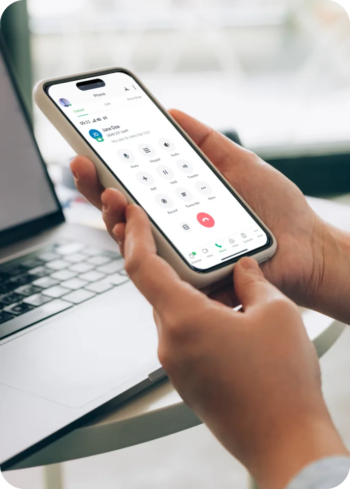 A person holding his phone making a call with a laptop behind him