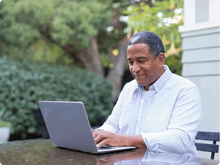 A man sits on a patio enjoying high-speed internet on a laptop on the table in front of him.