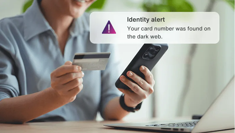 Woman holding a credit card and phone near a laptop, with an Identity alert popup warning card found on dark web.