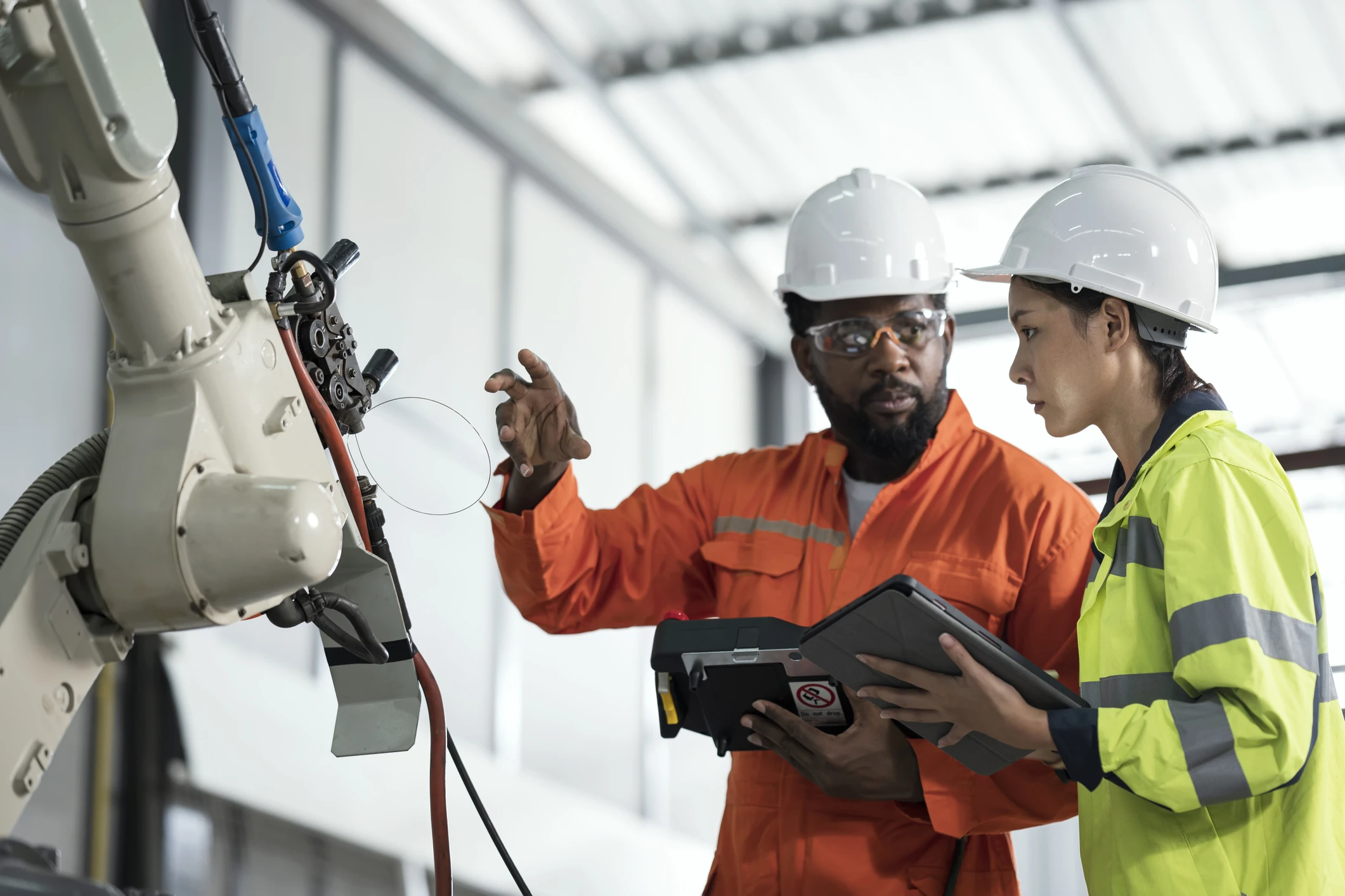 Two workers wearing hard hats examining a piece of machinery while holding IoT connected devices.