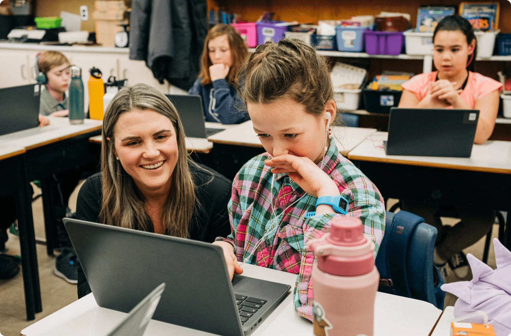Julia Rivard Dexter, founder of Shoelace, smiling next to one of her students while they play a game on their laptop.