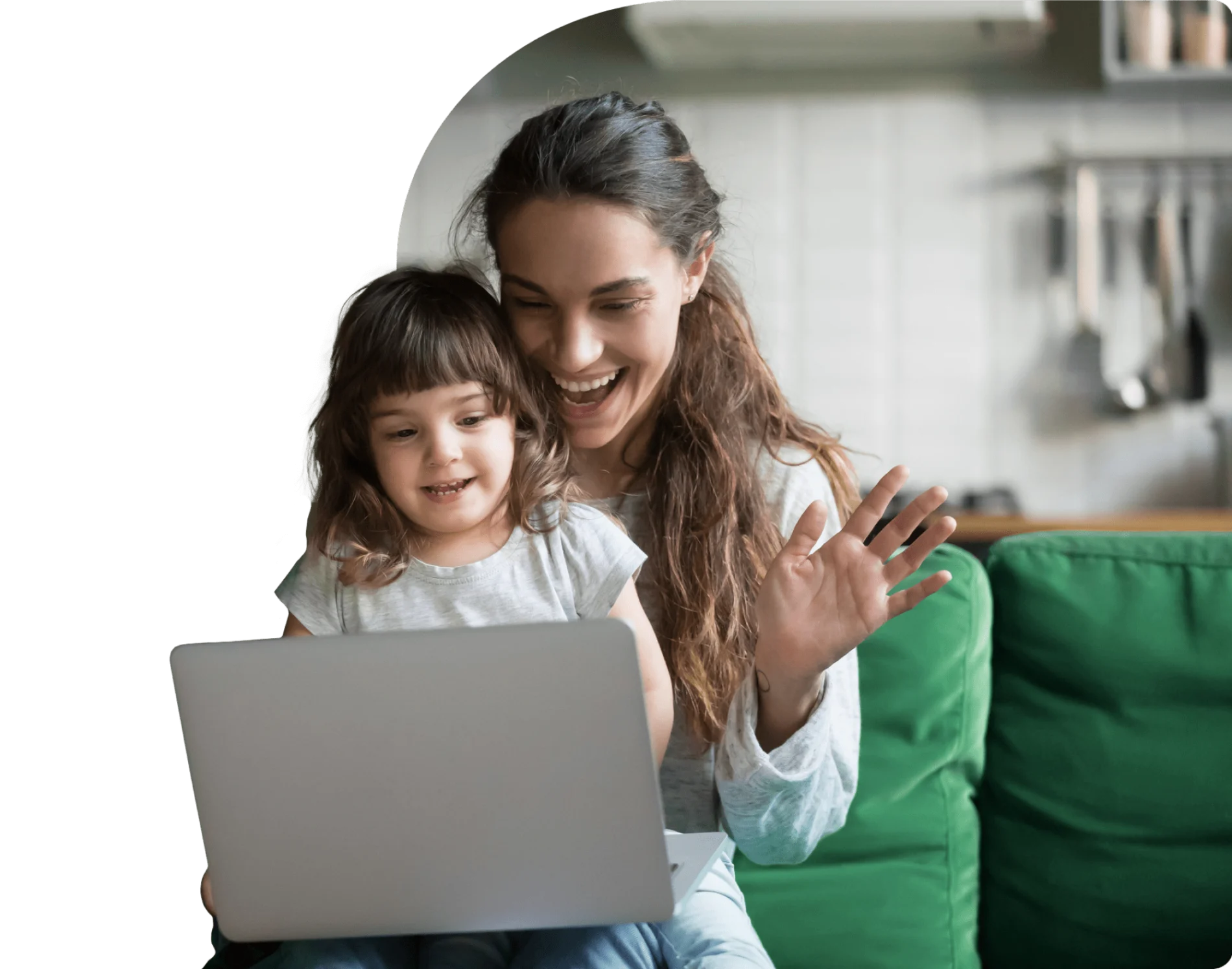 A mother and her daughter smile while viewing a laptop. The mother waves at the screen as they connect with family.