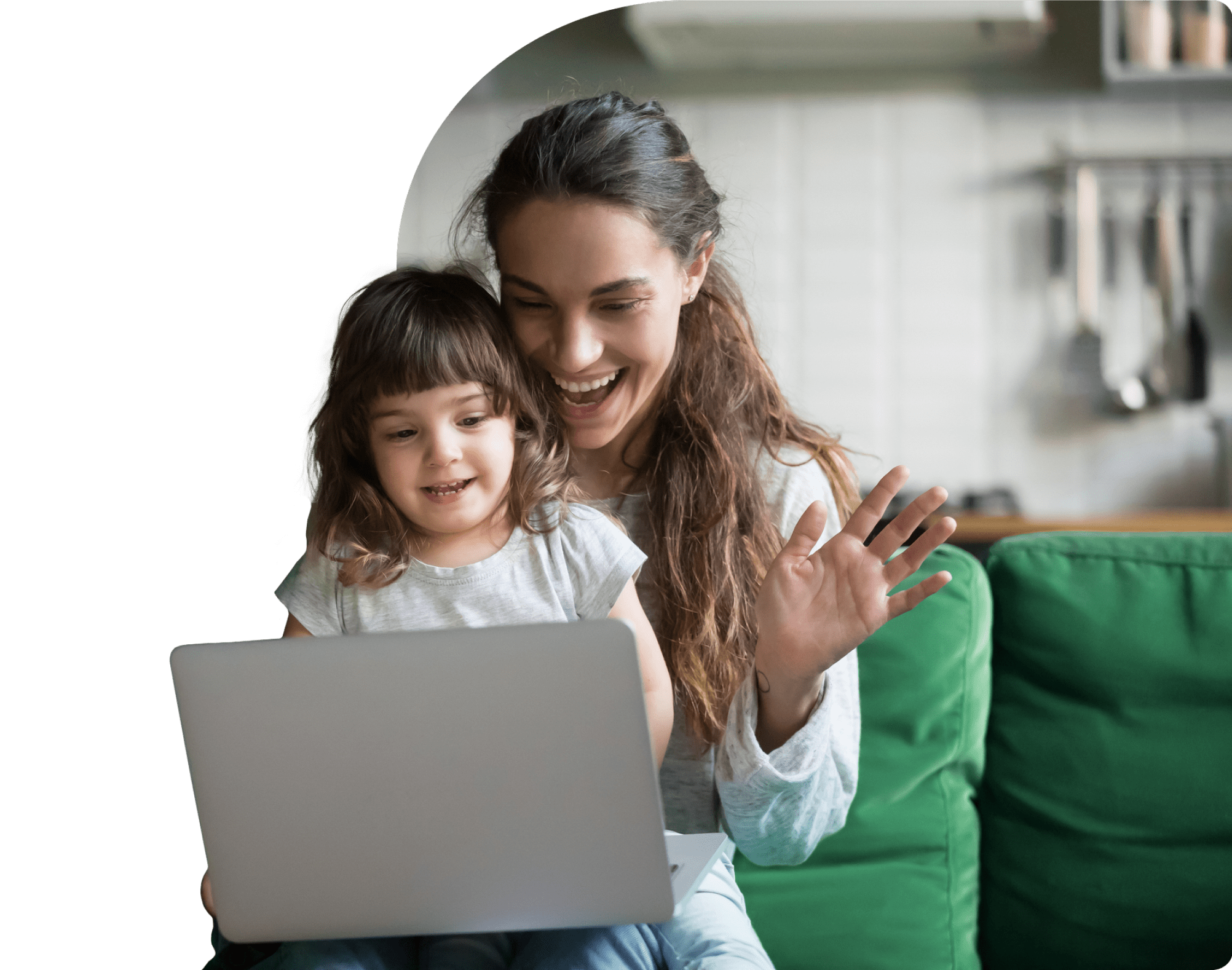 A mother and her daughter smile while viewing a laptop. The mother waves at the screen as they connect with family.