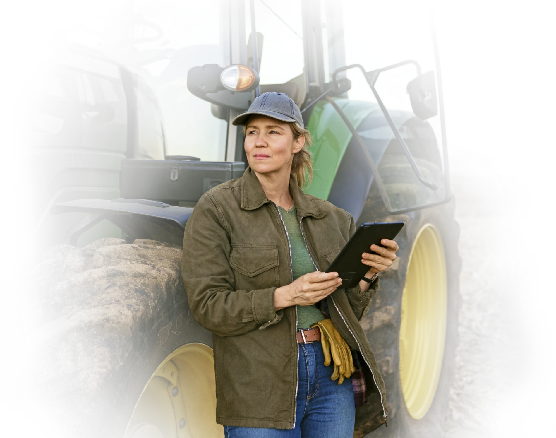 Une agricultrice tenant une tablette est  debout à côté de son tracteur dans un champ