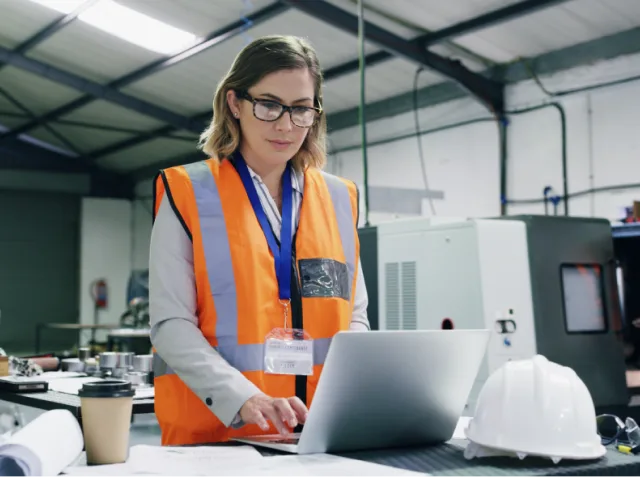 Connected worker wearing safety goggles and orange vest using laptop