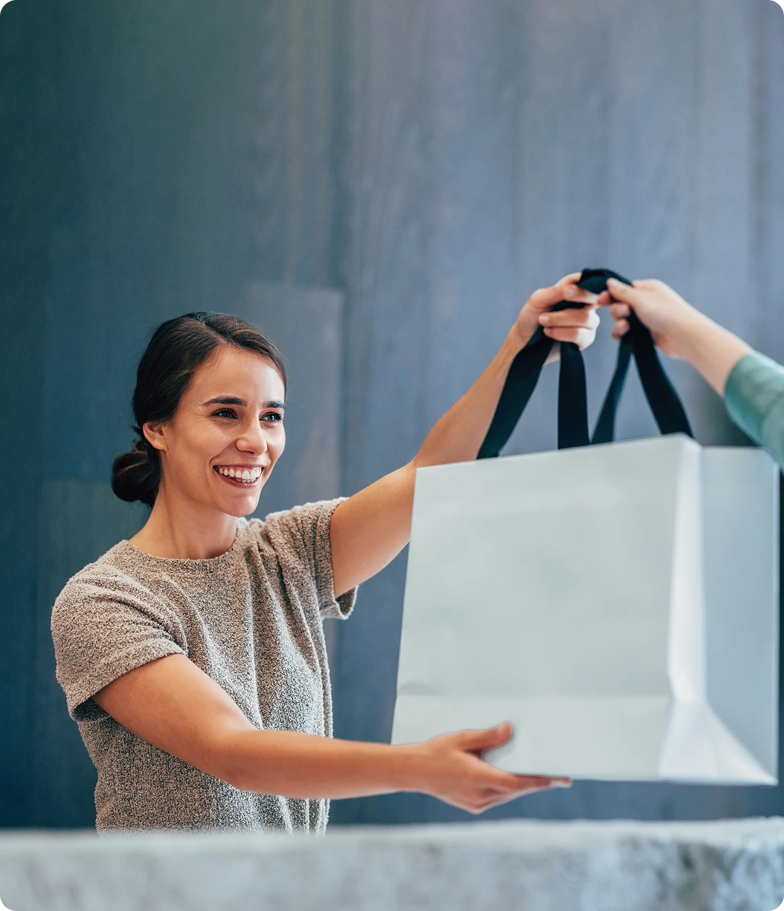 Retail clerk smiles while handing a large shopping bag to a customer.