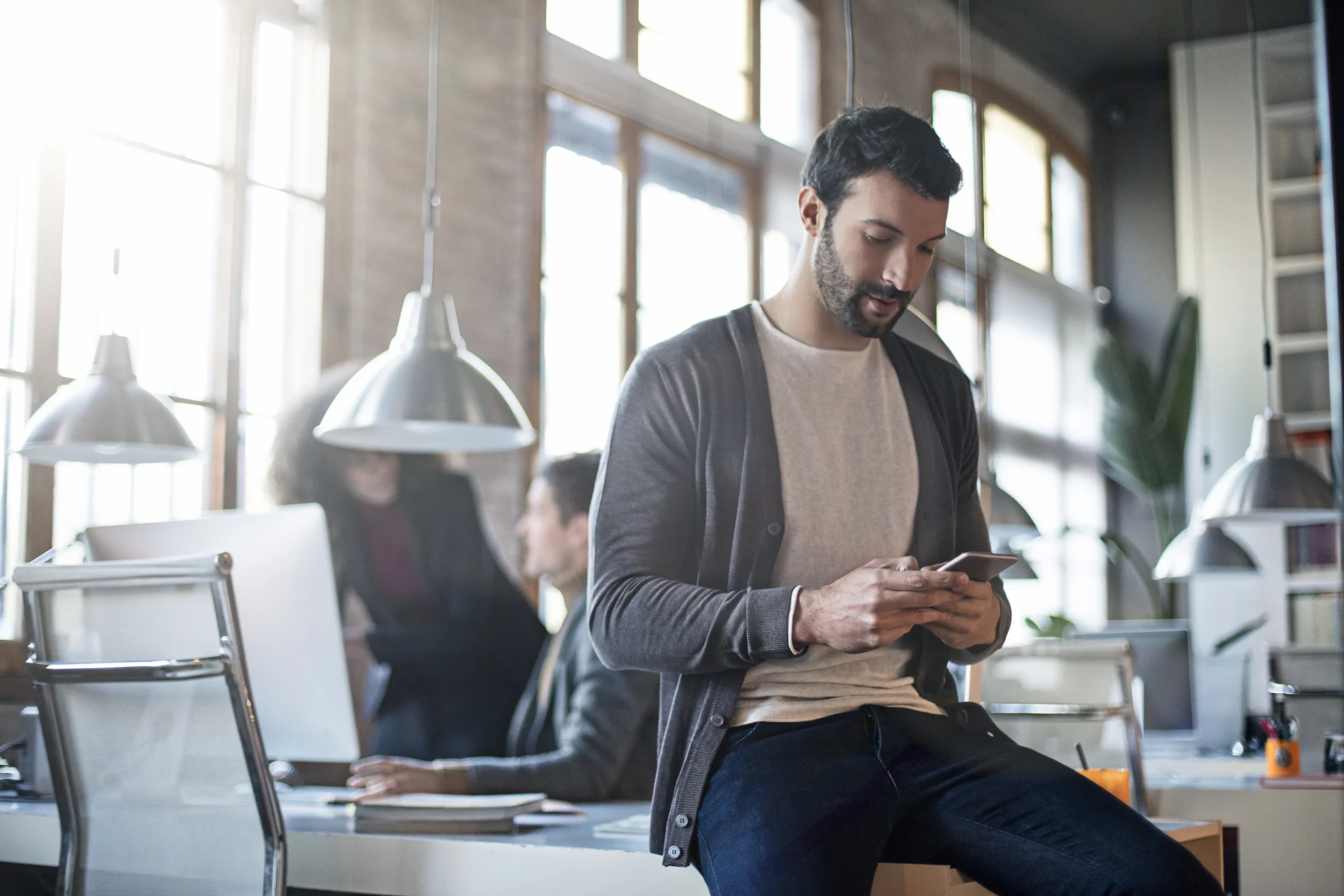 Une personne utilisant son téléphone intelligent, assise de manière décontractée sur un bureau dans un édifice de style industriel moderne.