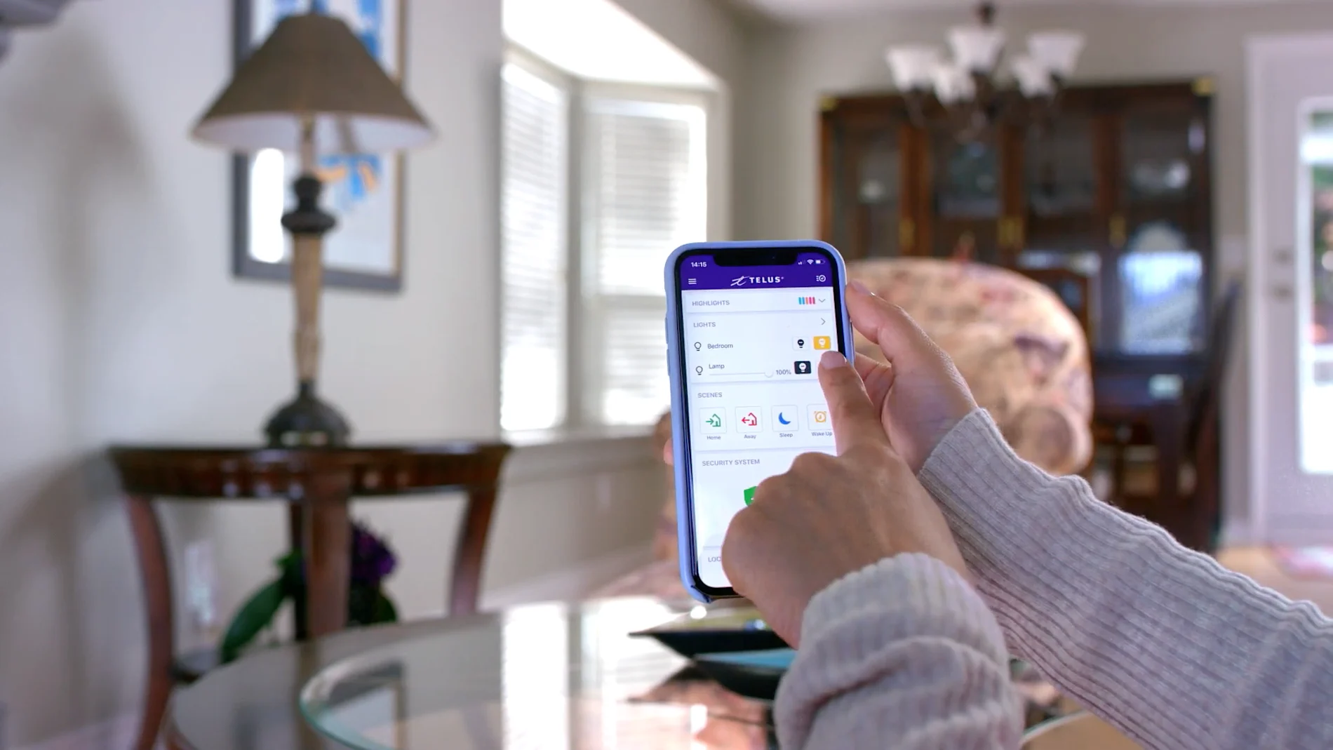 Hands holding a smartphone with the TELUS SmartHome app open for home monitoring.