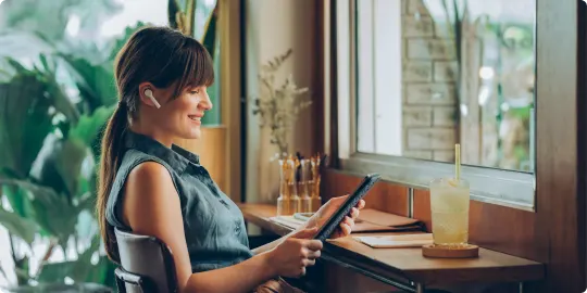Une femme assise dans un café regarde une émission sur sa tablette, symbolisant la vitesse et la couverture du réseau 5G de TELUS.