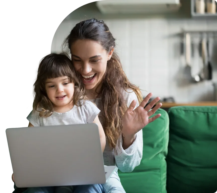 Une mère et sa fille regardent un ordinateur portable en souriant. La mère salue de la main un membre de la famille.