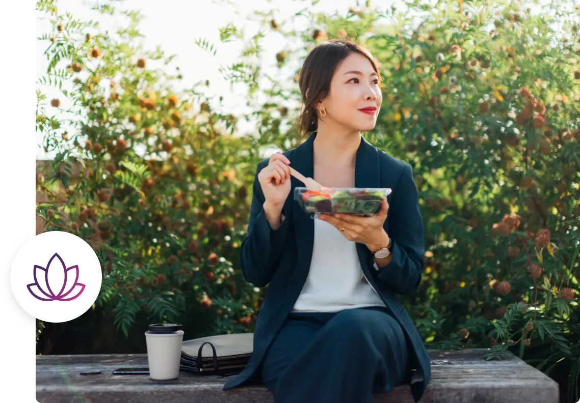 a professional female embraces wellbeing by sitting outside on a bench eating a salad