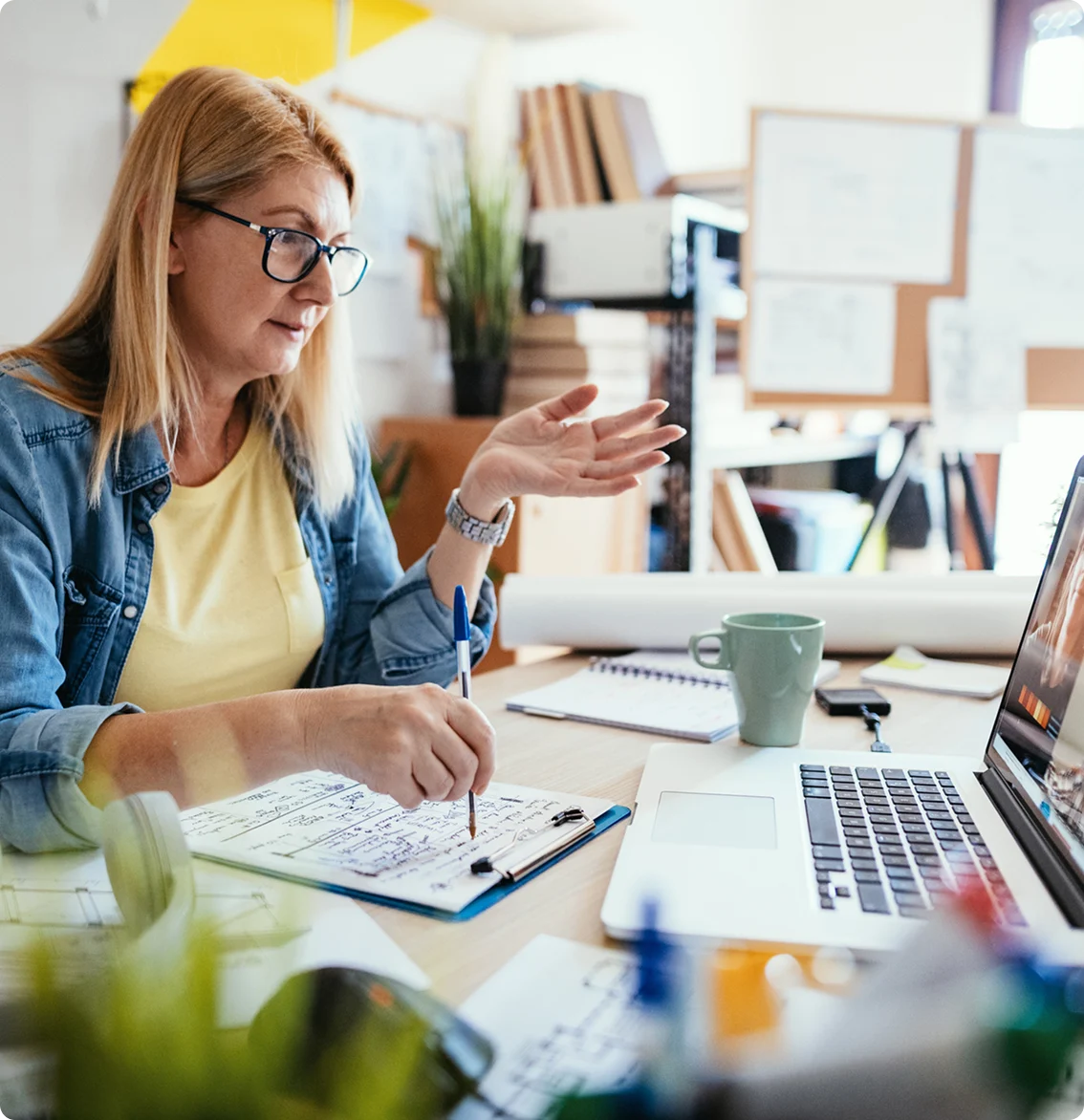 Professional woman on video call while taking notes at a home office desk.