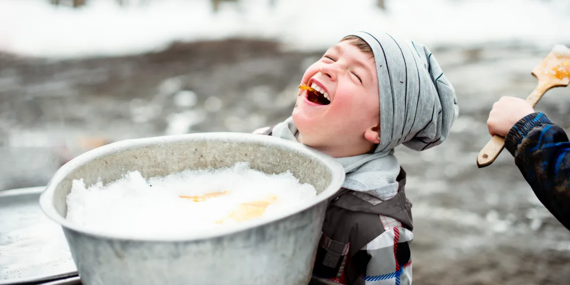 Child laughing while eating frozen maple syrup over a bucket of ice