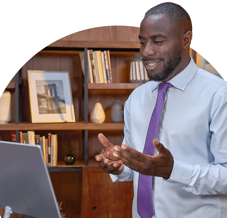 A man wearing a shirt and tie standing in front of a screen and speaking.