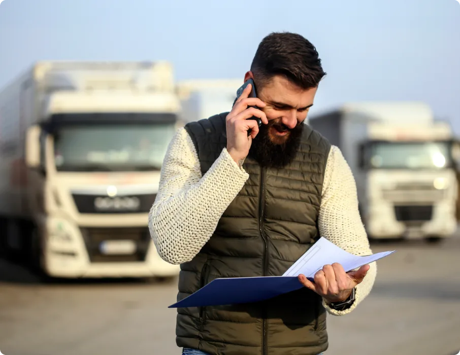 Fleet manager takes a call in a truck yard while reviewing papers.