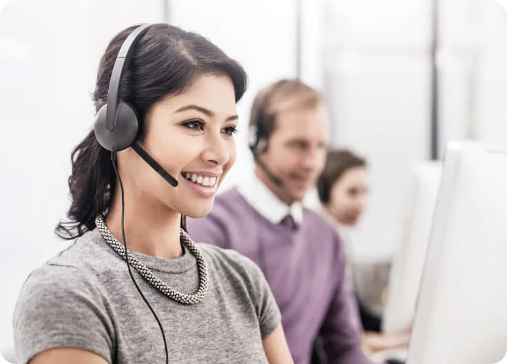 Three people wearing headsets happily answer calls at  a call-in support centre.