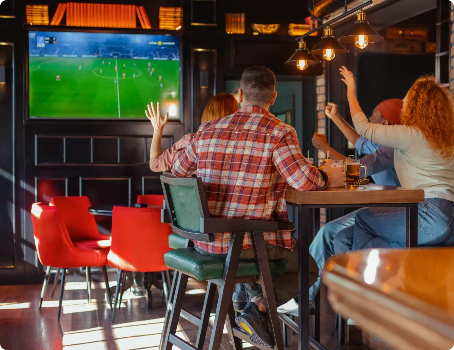 Customers watching soccer match on large TV screen in restaurant sports bar setting