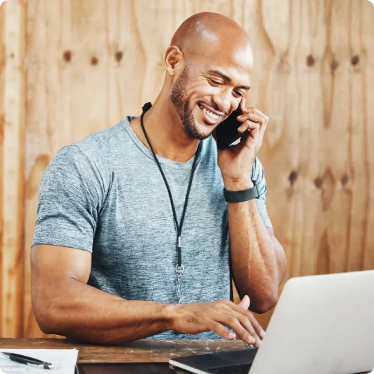 Fitness instructor smiles while taking a call and typing on a laptop.