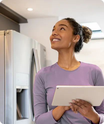 Woman with tablet in modern kitchen looking up thoughtfully