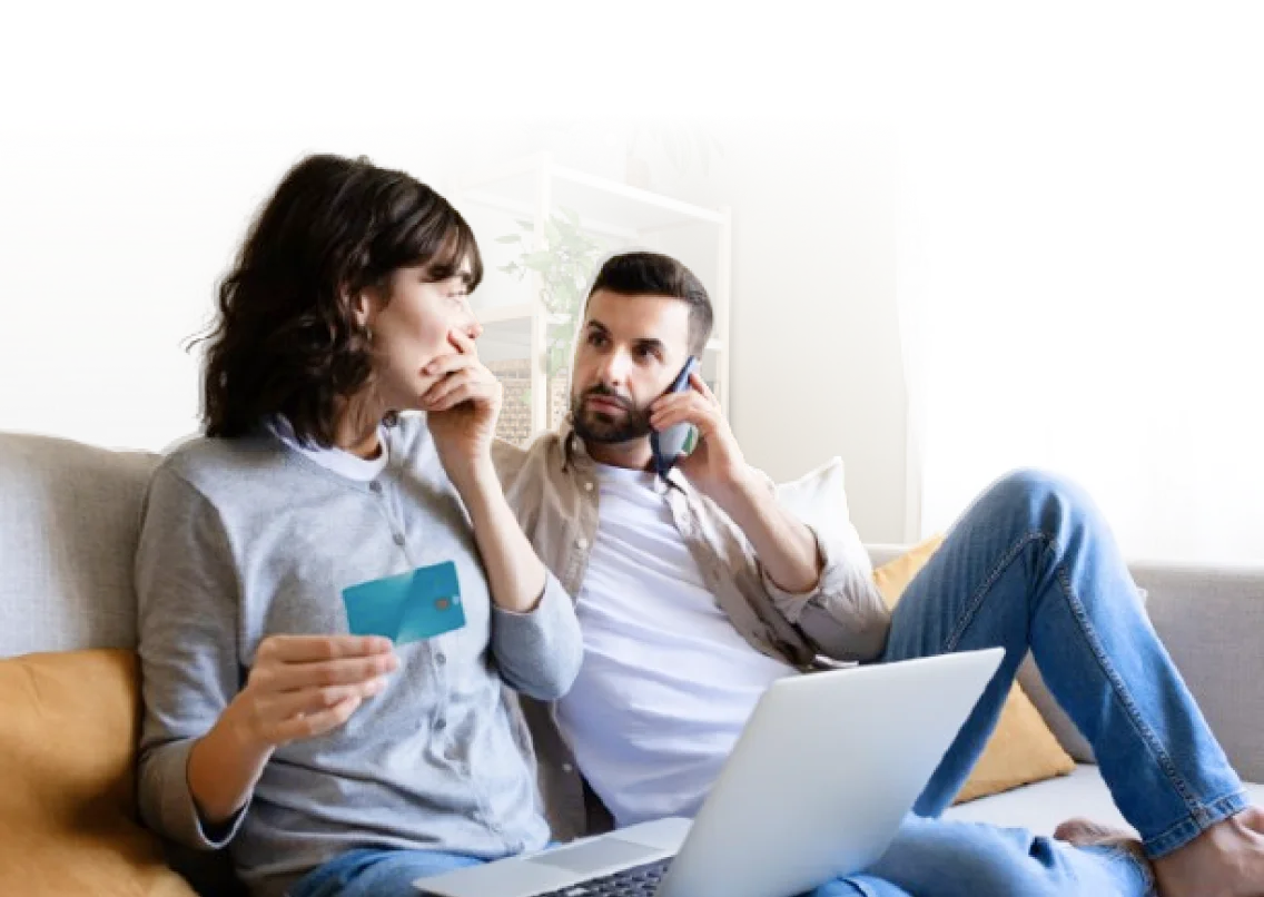 Two people checking out their credit card bill on laptop, the other one is conversing through phone.