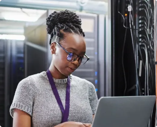 Field technician working in a server room, using a laptop to monitor and maintain network infrastructure, ensuring uptime and secure performance on-site.