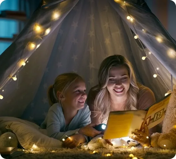 Children reading together under string lights in cozy tent