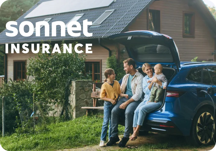 A family sitting in the trunk of their car outside their home.