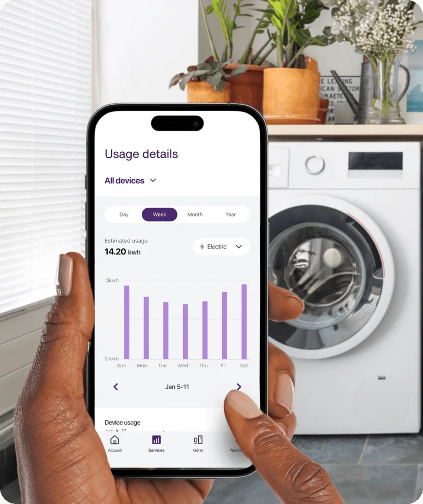 Hand holding smartphone showing appliance energy usage near washer/dryer