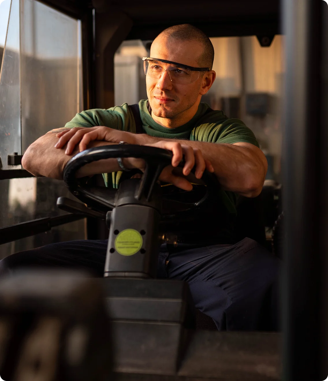 Forklift operator rests hands on the wheel, looking ahead.
