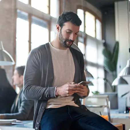 Homme dans un bureau lumineux consulte son téléphone intelligent assis sur un bureau.