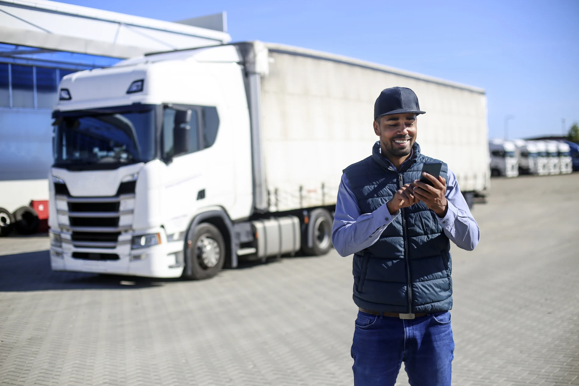 Man, smiling, standing in front of a fleet vehicle, using a mobile device